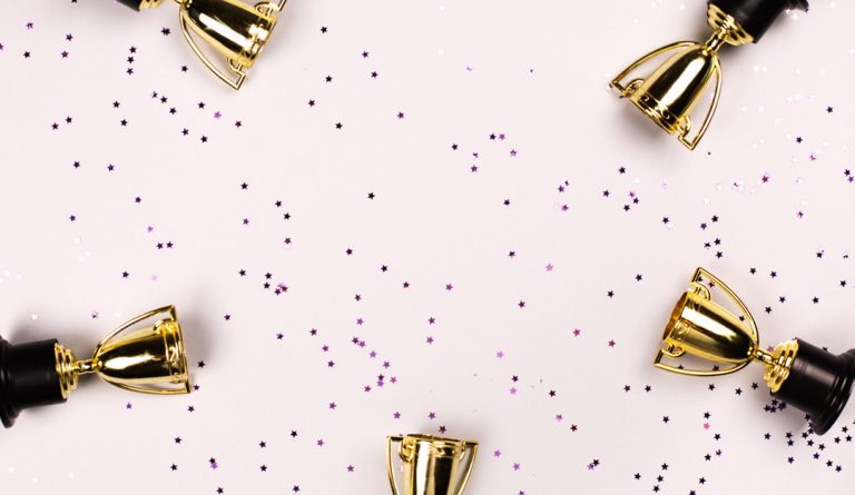 five trophies against a pink background with confetti