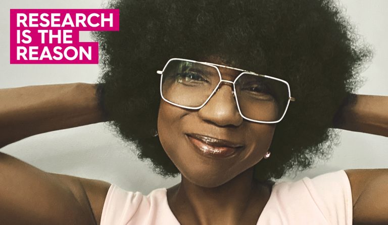 portrait of suzette simon wearing an afro wig and smiling at the camera in a pink top