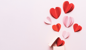 cut outs of red and pink paper hearts against a light pink background||