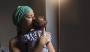 A woman with breast cancer wearing a scarf holds her baby