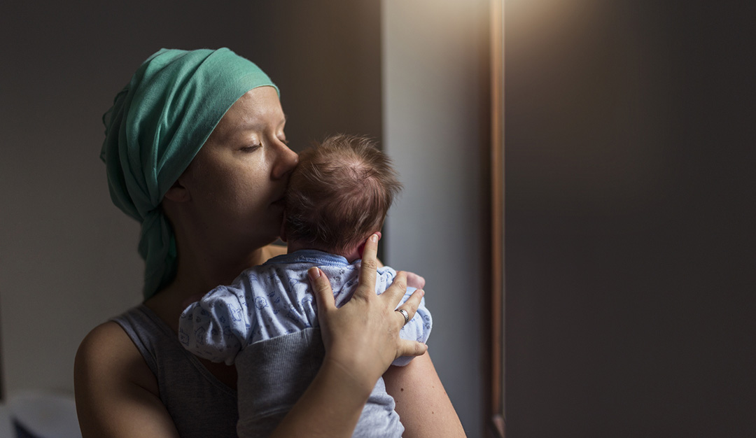 A woman with breast cancer wearing a scarf holds her baby