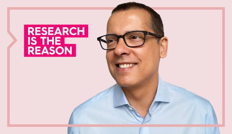 a portrait of andre wearing a light blue shirt against a light pink background smiling
