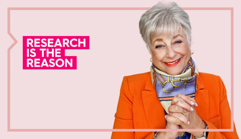 Ellen wears an orange blazer and smiles at the camera against a light pink background
