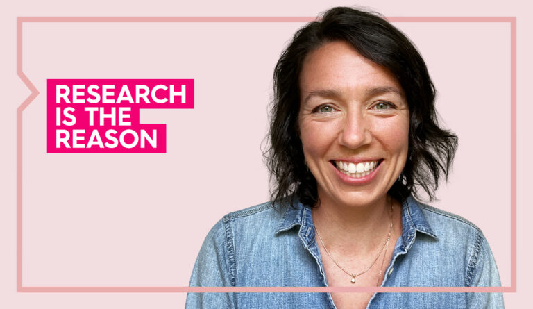 Lauren wears a blue shirt and smiles at the camera against a light pink background