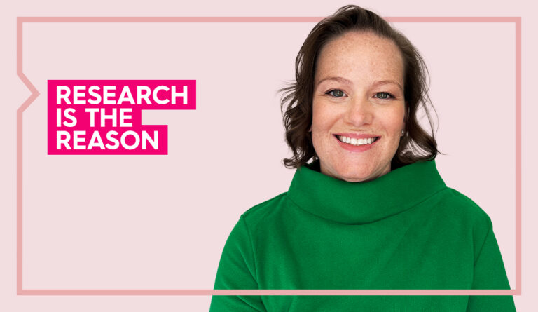 Clara wears a green turtleneck and smiles at the camera against a light pink background