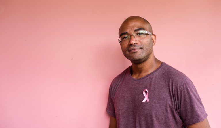 portrait of a black man wearing a maroon shirt with a pink ribbon on his chest, evokes male breast cancer