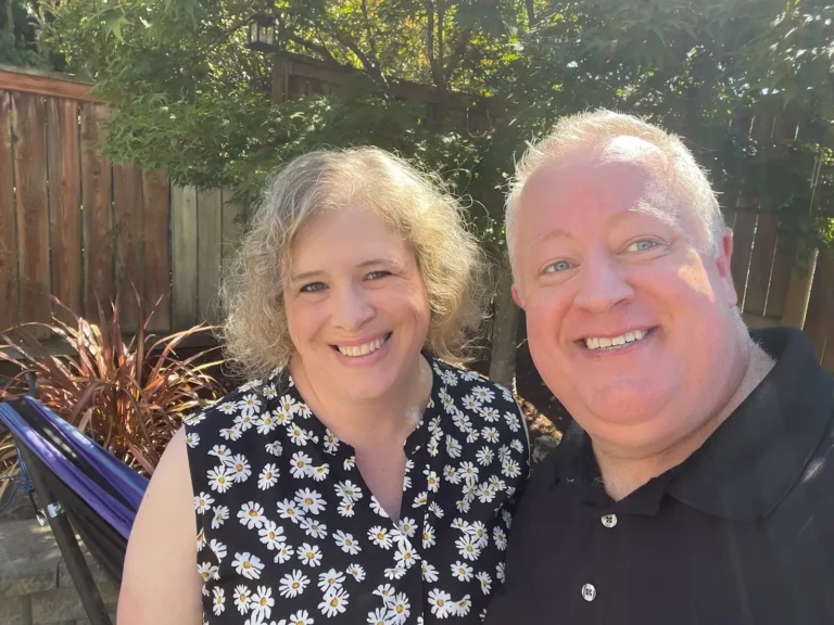 a woman and a man smiling for the camera in front of a tree in a backyard